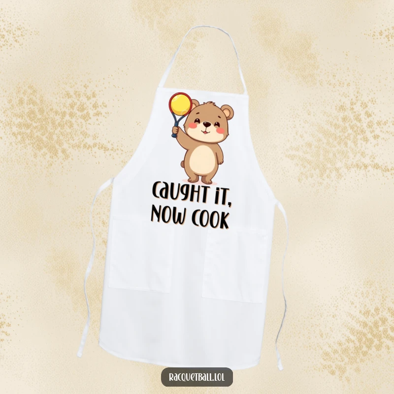 Funny Apron: Curious bear character triumphantly holding a tiny racquetball, bringing sports humor to the kitchen.