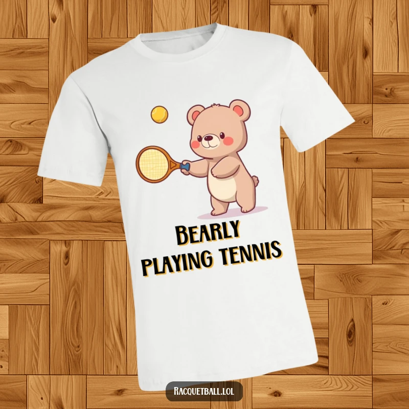 Funny t-shirt featuring a small bear humorously using a giant tennis racquet to playfully swat a bouncing ball upwards, showcasing determination.