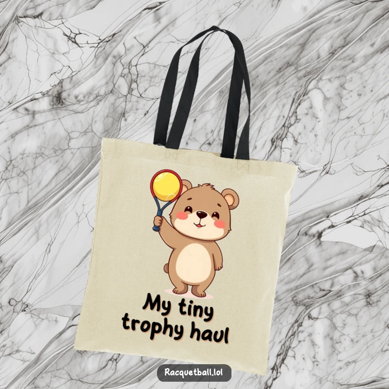 Funny Tote Bag: Curious bear character triumphantly holding a tiny racquetball, perfect for carrying sports essentials comically.
